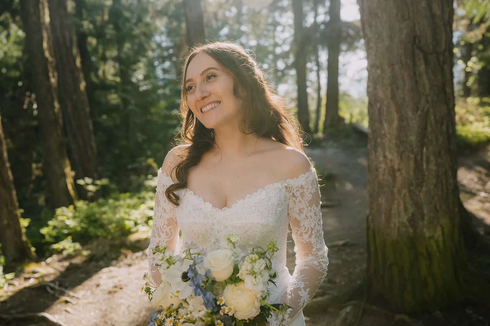 Bruna in the forest Bruna smiling up into golden dappled sunlight on a forest trail, holding a bouquet of white roses, blue delphiniums, and wild flowers