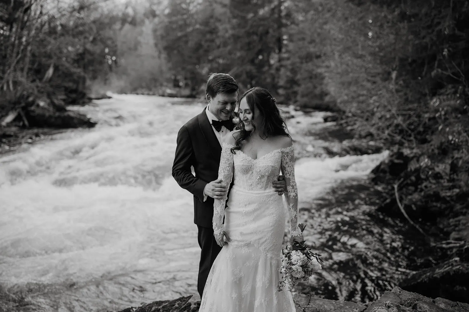 By the river Black and white β James nuzzling Brunaβs cheek as they both grin, standing beside a fast-flowing glacial river in the Whistler forest