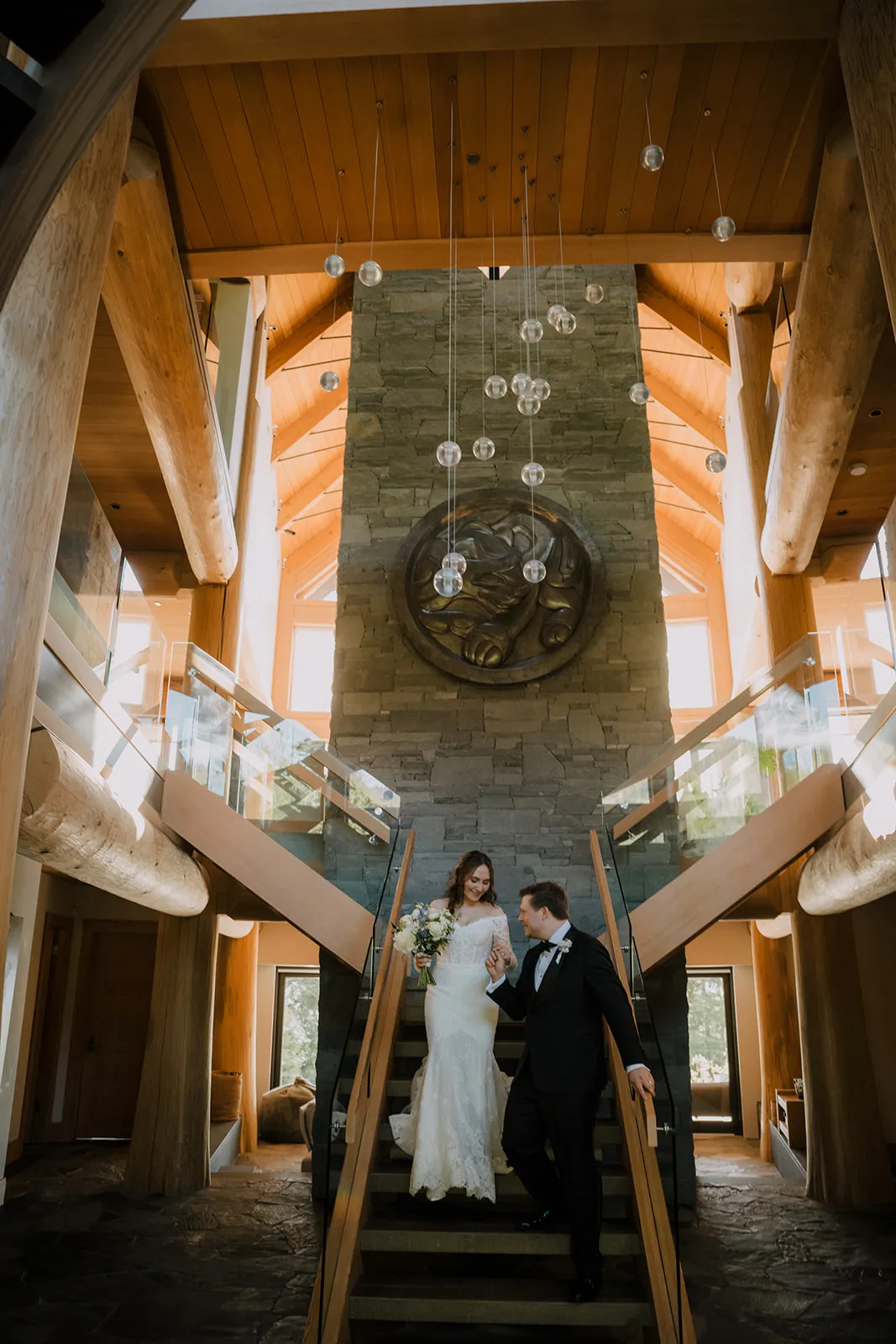 Grand entrance James leads Bruna down a sweeping staircase inside the timber-framed lodge, laughing together beneath a cascade of hanging glass globe lights